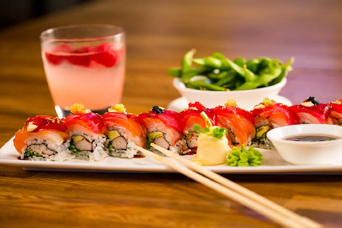 Plate of sushi accompanied by sauces and salads, and a pink drink, with chopsticks on it