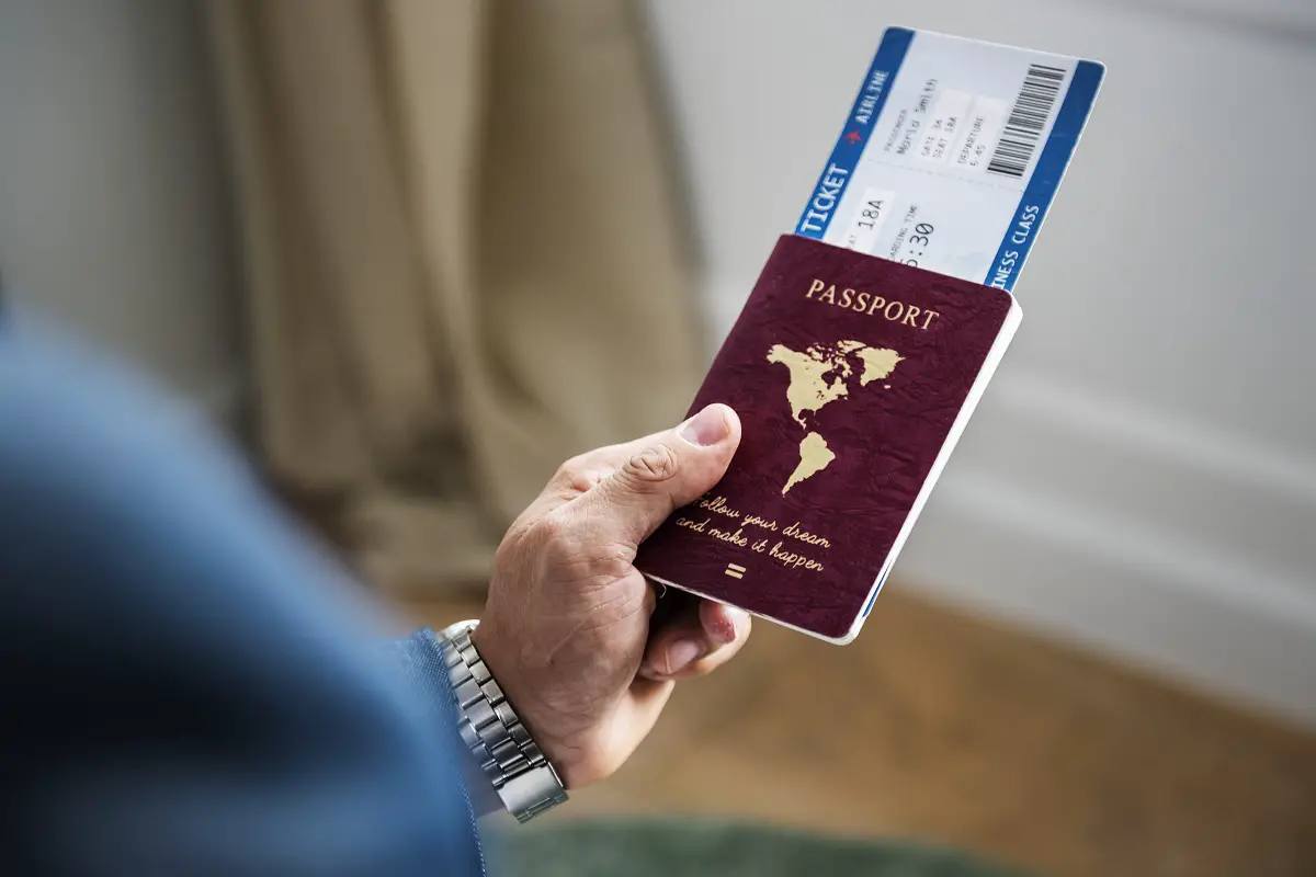 Pessoa segurando seu passaporte com mão esquerda, bem como passagem dentro da mesma, após conseguir seu Visto americano para viajar para os EUA